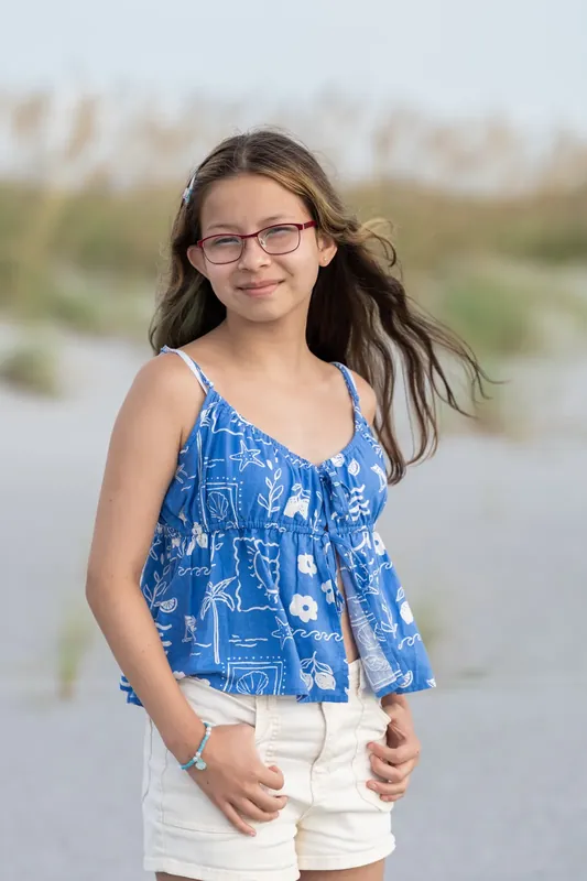 Teen wearing glasses and a blue patterned top stands on the sand at Vilano Beach in St. Augustine.