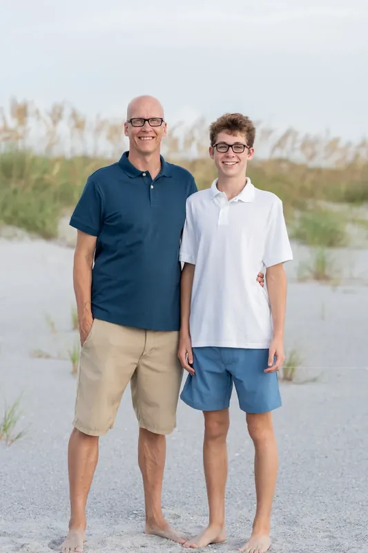 Two males in casual summer clothing face the camera on the sand at Vilano Beach.