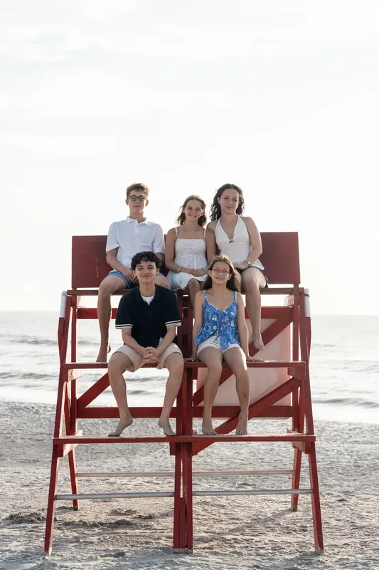 An extended family line stands along the shoreline at the beach, the group stretching across the frame in casual clothing.