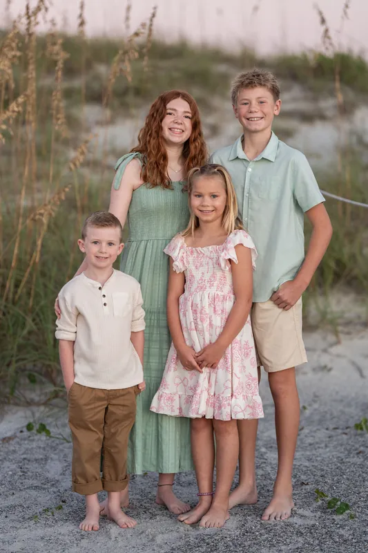 Four children stand together on the sand at Vilano Beach, wearing coordinated pastel outfits in cream, green, and pink tones.