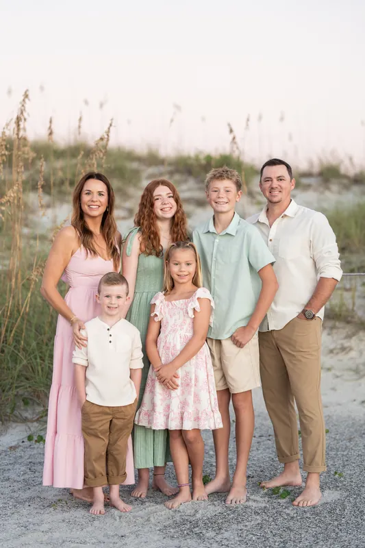 Two adults and three children pose together on the beach at Vilano Beach in soft neutrals and pastels, with dunes behind them.