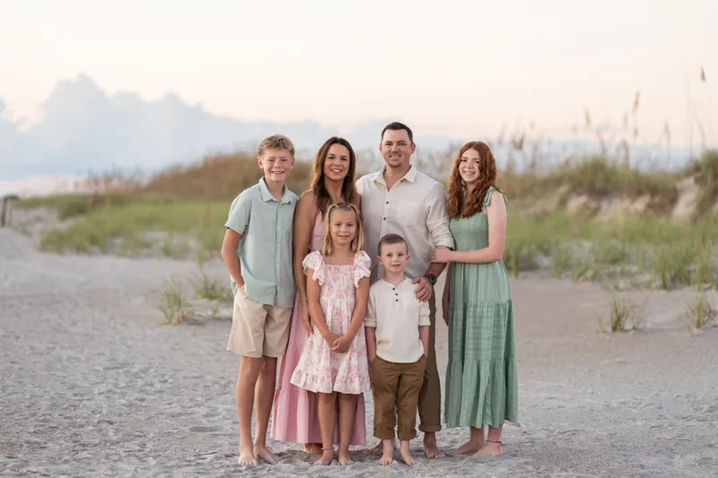 Group of six pauses on the beach at Vilano Beach as golden hour light bathes the dunes behind them.