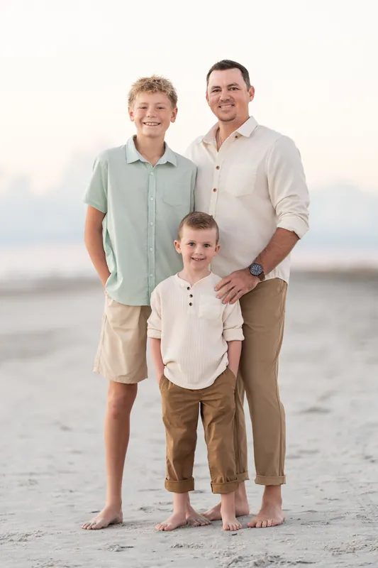 Two adults and three children stand barefoot on the sand at Vilano Beach, ocean visible behind.