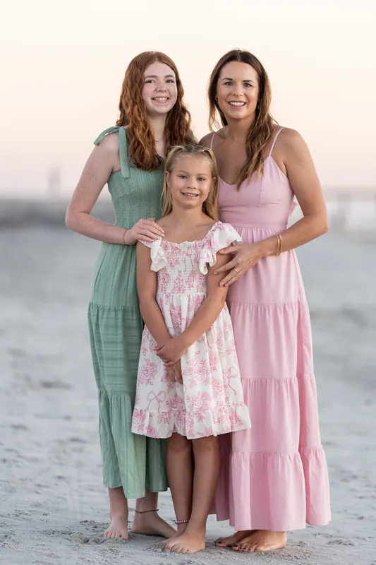 Two women and a child in pink and green dresses pose together on the beach at Vilano Beach.