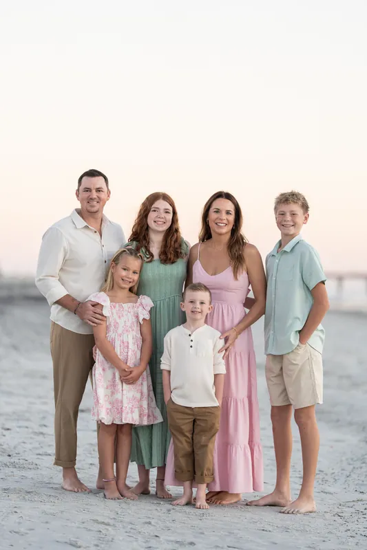 Extended family group of seven arranged on the sand at Vilano Beach with calm water in the background.