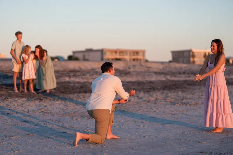 A small group spreads across the beach while one person kneels in the foreground, all in pastel clothing at golden hour.