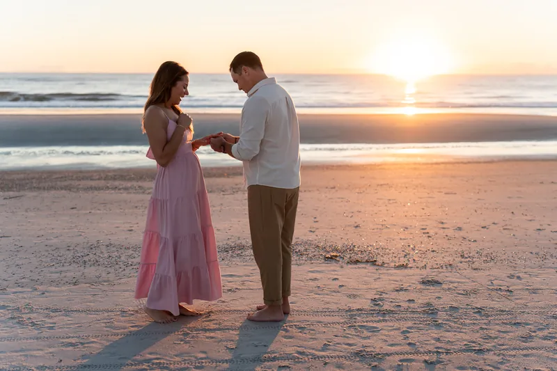 Two people exchange rings on the wet sand with the ocean and sunrise glowing behind them at Vilano Beach.