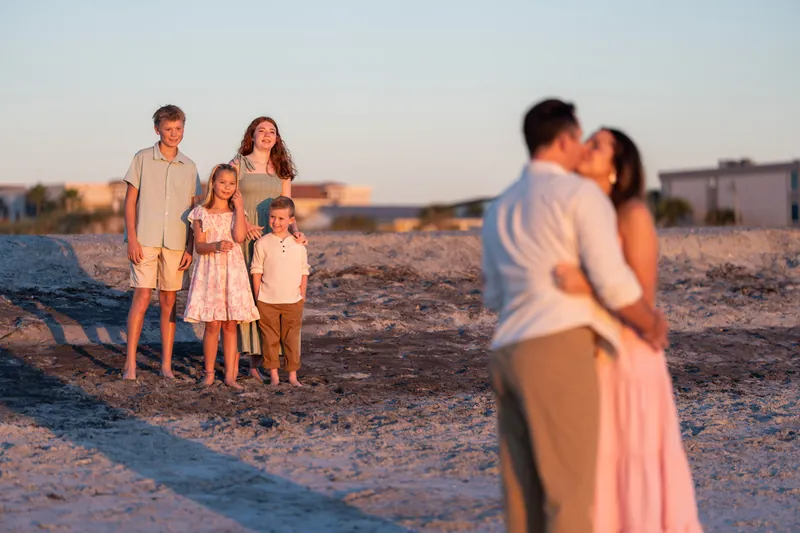 A couple in the foreground kisses as family members stand together further back on the beach at Vilano Beach.