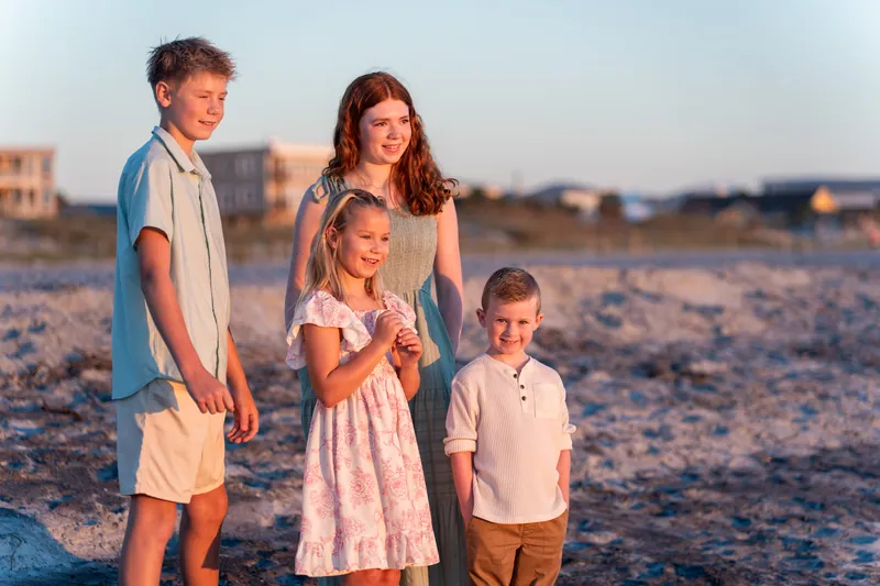 Four children in casual beachwear stand together on the sand at Vilano Beach with the sunset sky behind them.