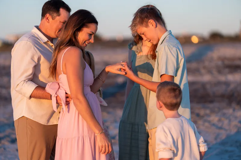 Adults and children gather in a circle on the beach at Vilano Beach, exchanging a moment together at dusk.