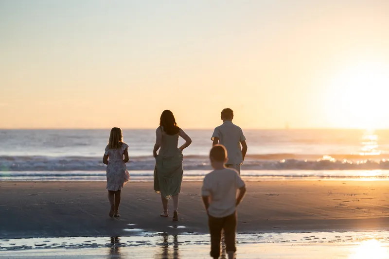 Three children wade in the shallow water at Vilano Beach, facing the ocean as the sun sets on the horizon.