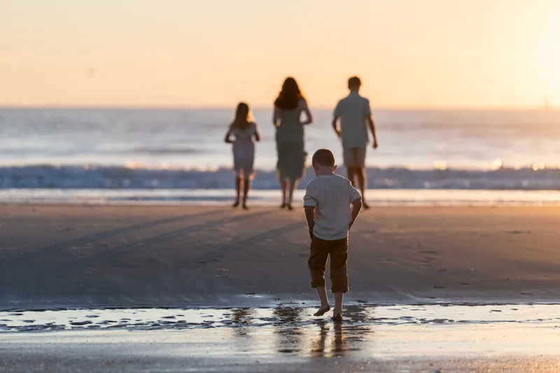 One child wades into the Atlantic while four people stand on the sand at Vilano Beach at sunset.