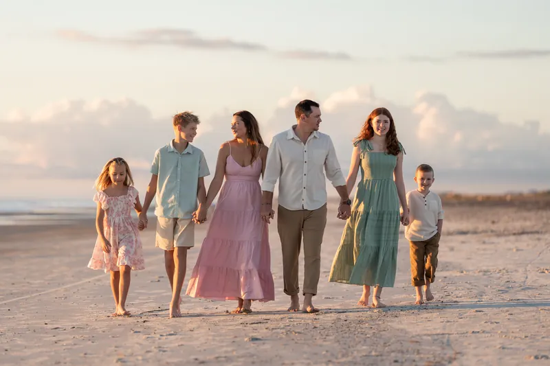 Six people walk hand-in-hand across the wet sand at Vilano Beach in coordinated casual clothing at golden hour.