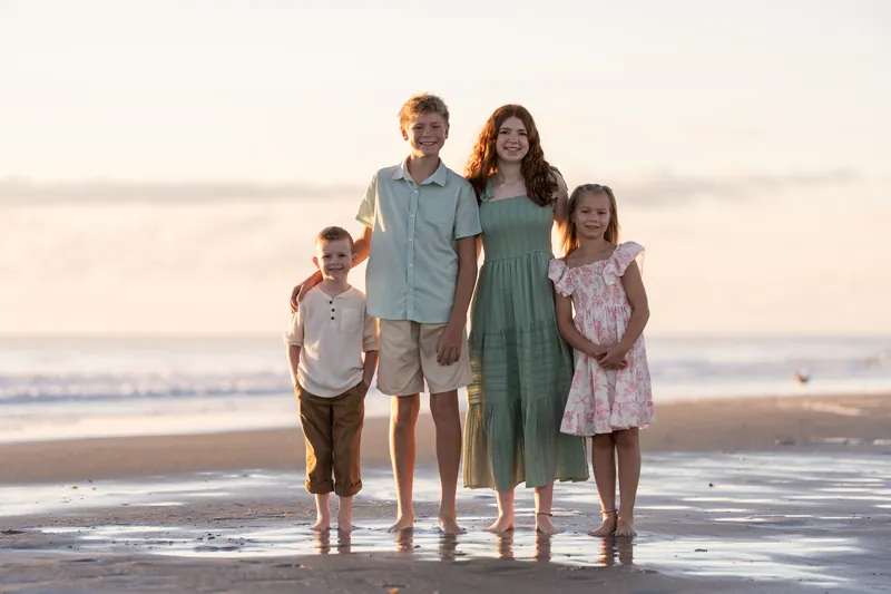 Four children and two adults stand in a line on the wet sand at Vilano Beach, all facing the camera with the ocean behind them.