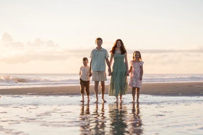 Five people stand together in shallow water at Vilano Beach at dusk, their reflections visible in the wet sand beneath them.