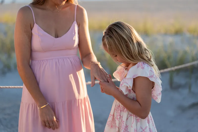 Adult in pink dress holds hands with a young child in matching pink at Vilano Beach as golden light filters through beach vegetation.