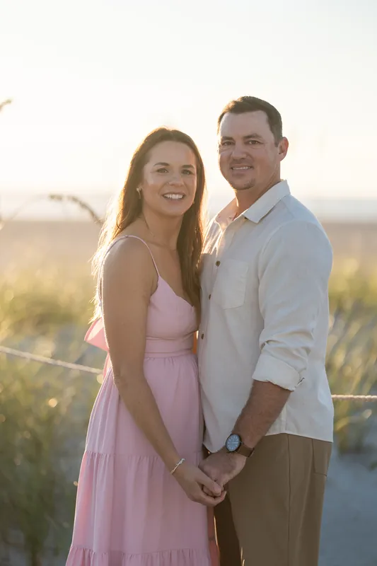 Kelly and Jereme hold hands at sunset overlooking Vilano Beach's salt marsh, she in a pink dress and he in a light blue shirt.