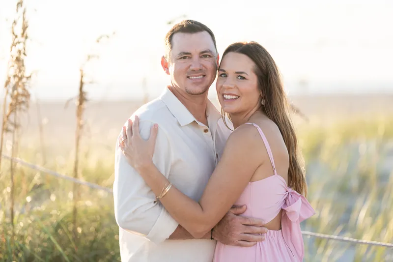 Two people in casual embrace among tall grasses at Vilano Beach, golden light illuminating the marsh behind them.