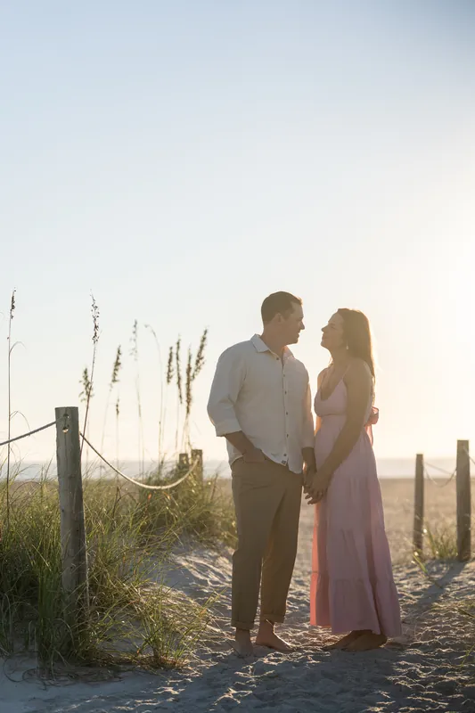 Kelly and Jereme hold hands on a sandy path lined with dune grasses and wooden posts at Vilano Beach at golden hour.