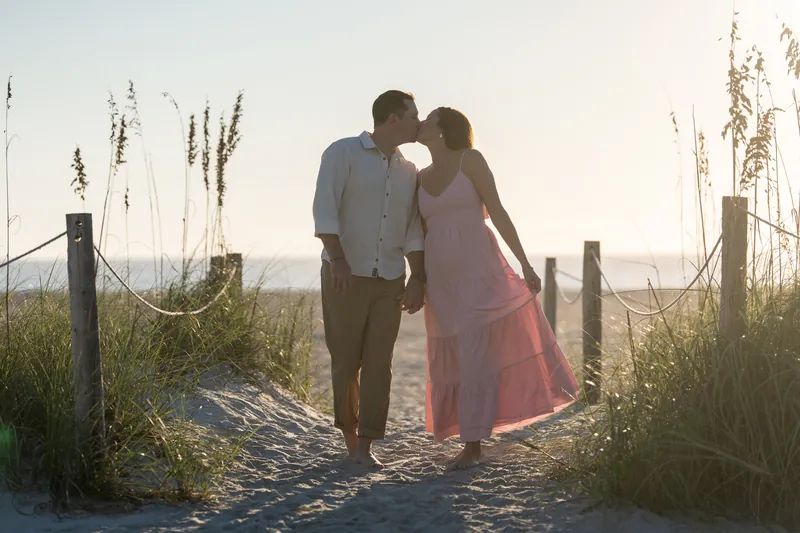 A couple kisses on a sandy trail bordered by coastal vegetation and weathered wooden markers at Vilano Beach.