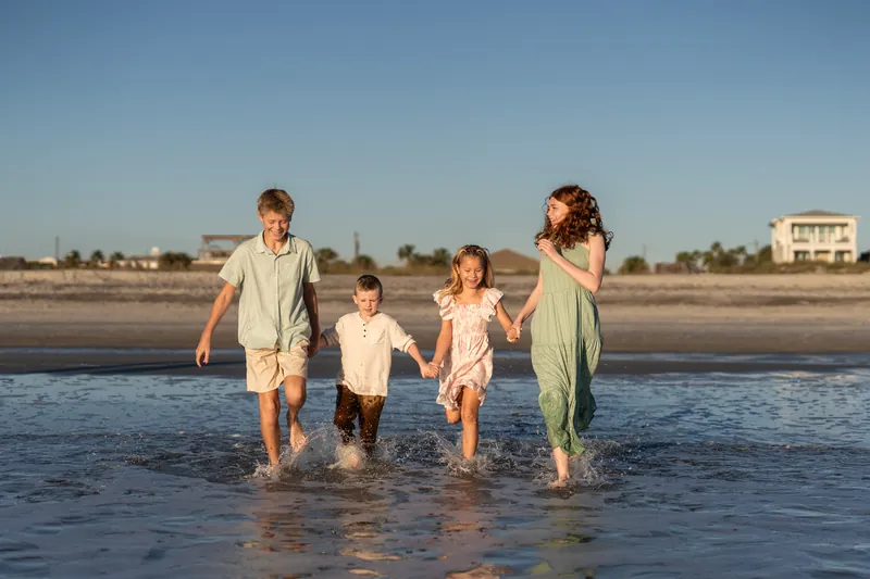 Four people wade into shallow water at Vilano Beach under clear skies, wearing soft pastels.