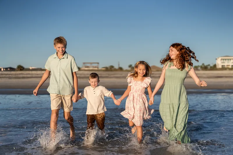 A group of four runs through knee-deep surf at Vilano Beach, splashing and laughing together.