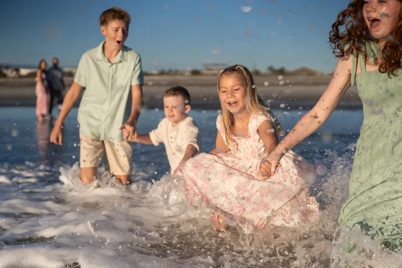 Four family members play in the waves at Vilano Beach, with one child lifted mid-leap into the foam.