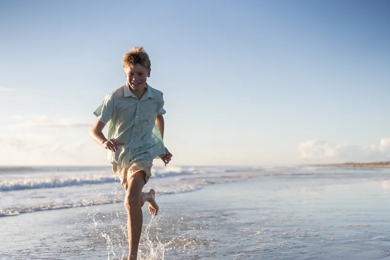 A young person jogs along the shoreline at Vilano Beach, kicking through the surf.