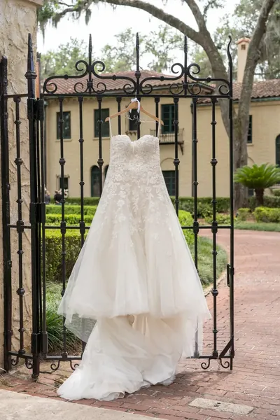 Wedding dress displayed on hanger at ornate iron gate with historic mansion
