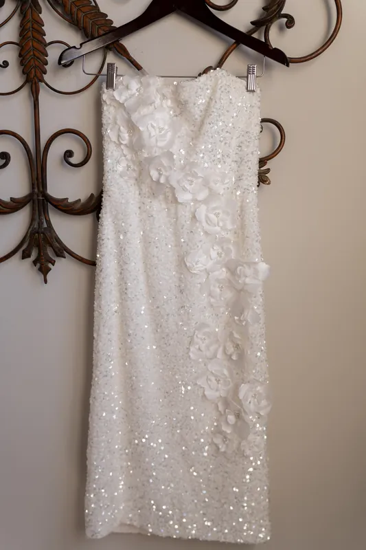 Sleeveless white sequined dress with floral beading hangs from ornate scrolled metal wall fixture at Casa Monica Resort &