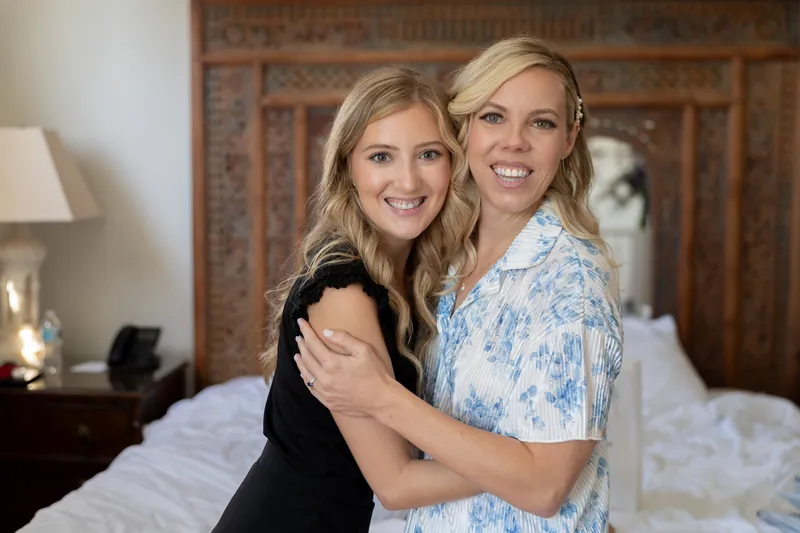Kerry and companion embrace and smile at camera in bedroom with ornate wooden headboard at Casa Monica Resort & Spa.