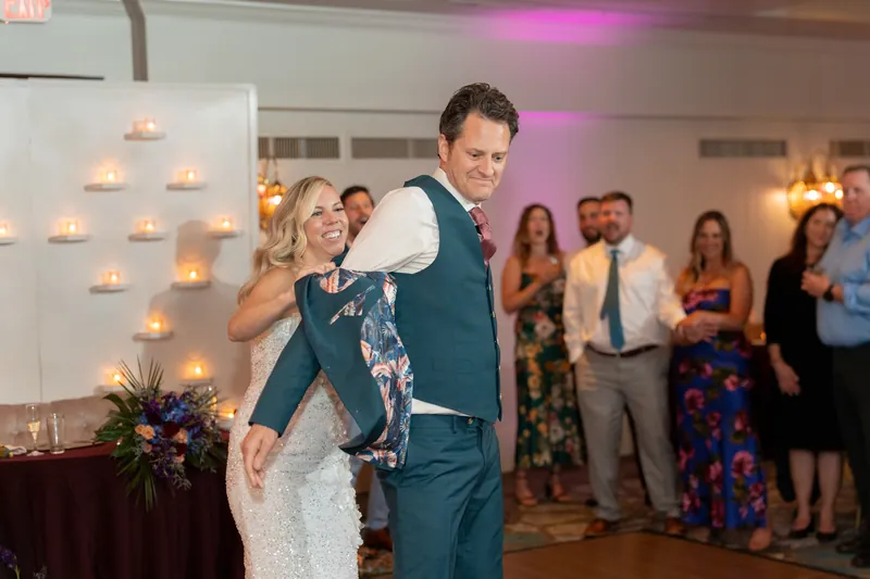 Kerry wraps their arms around Rhett's neck as he holds them during a romantic dance moment with guests looking on.