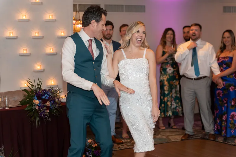 Kerry and Rhett dance cheek-to-cheek on the wooden floor with guests gathered around them in the illuminated ballroom.