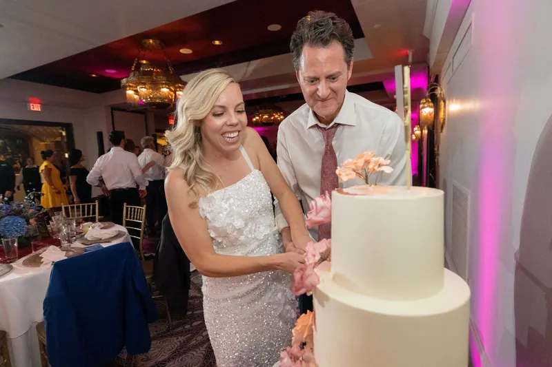 Kerry and Rhett cut into a white tiered cake, both smiling as they hold the knife handle together.
