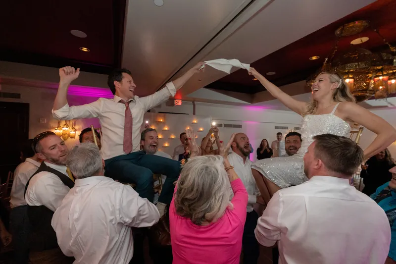 Guests dance with their hands raised, forming a circle around the couple on the dance floor.