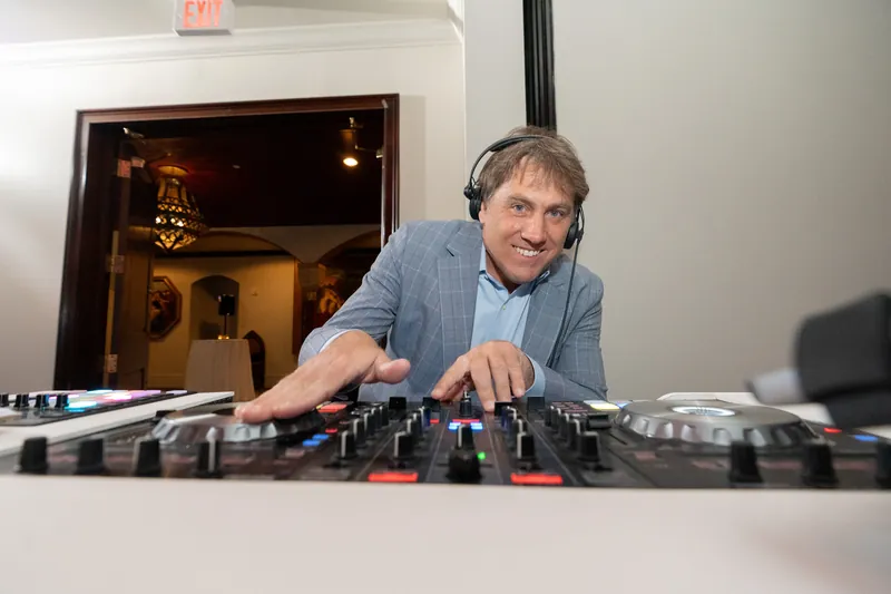 A DJ in a light blue shirt operates turntables at Casa Monica Resort & Spa, smiling at the camera.
