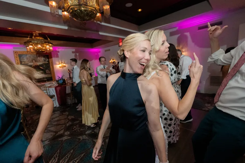 A blonde woman in a black halter top dances with guests under purple lighting.