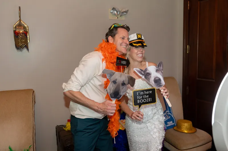 Rhett and a companion wear feather boas and novelty hats while posing with a photo booth prop.