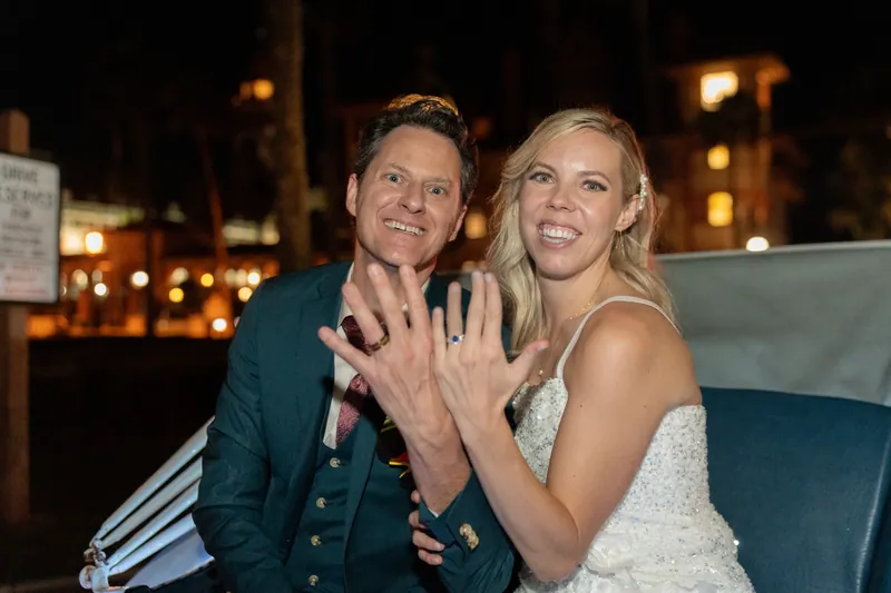 Kerry and Rhett display their wedding rings to the camera, both smiling with the resort's lit courtyard visible behind them.