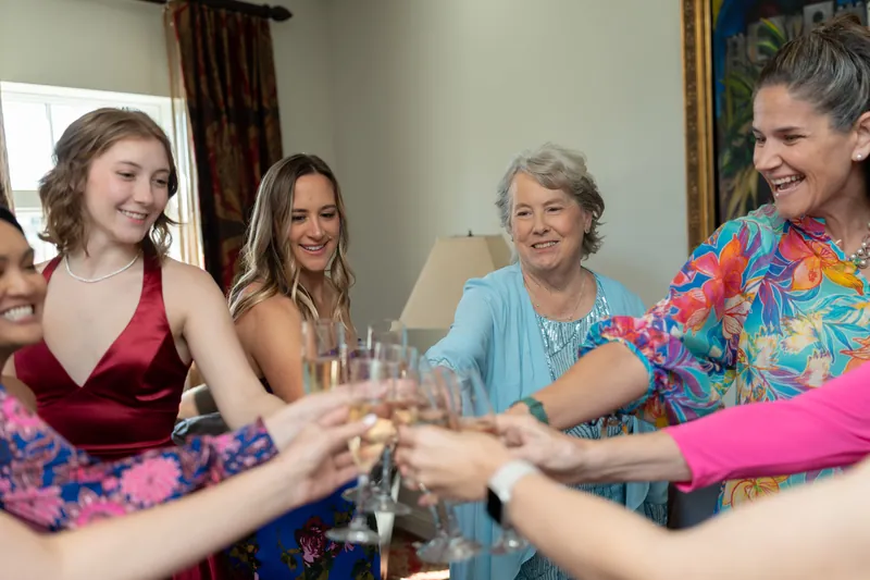 Five people of varying ages clink glasses together during a wedding celebration indoors.