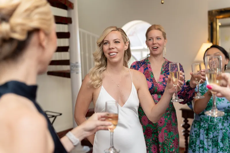 Kerry smiles while holding a champagne flute surrounded by guests in colorful patterned dresses at Casa Monica Resort & Spa.