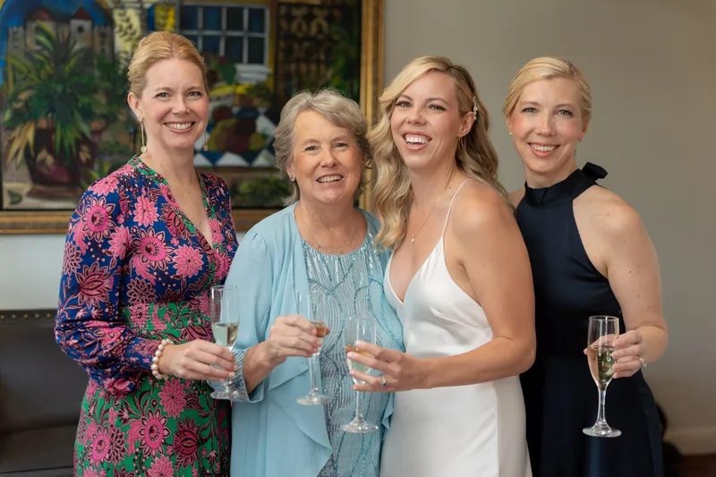 Four women stand together smiling, holding champagne flutes in front of a colorful framed painting at Casa Monica Resort &