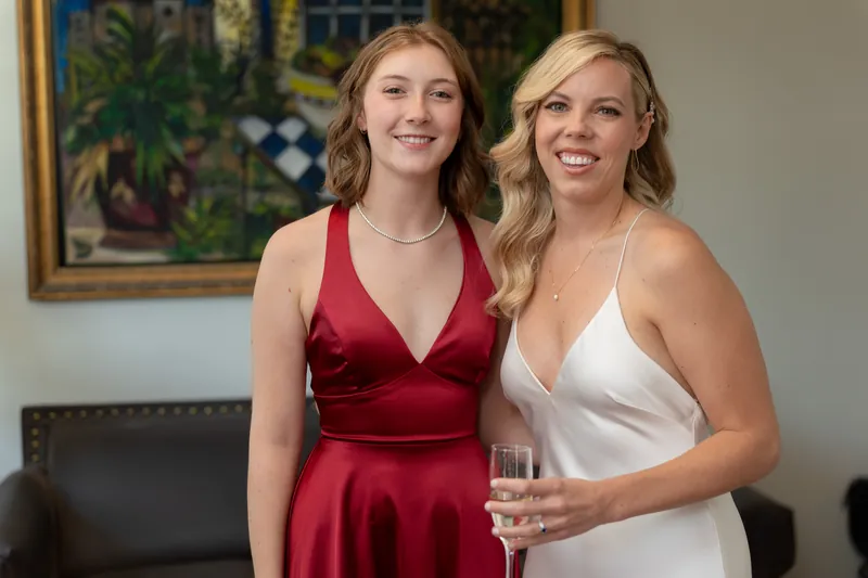 Rhett's companion in a burgundy dress and Kerry in white hold champagne glasses, posing together at the reception.