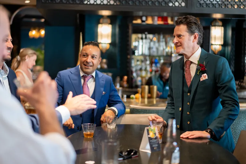 Rhett chats with guests at the bar, flanked by two other men in suits during the celebration.