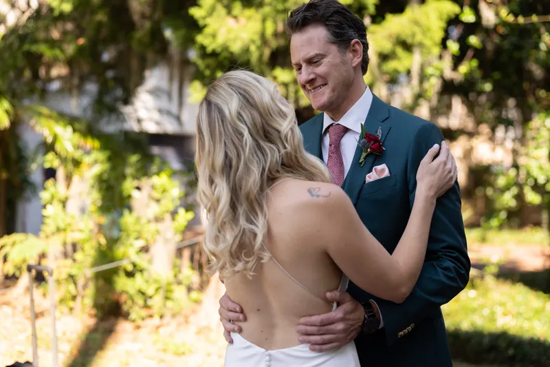 Kerry and Rhett embrace while smiling at each other in dappled sunlight among the resort's lush landscaping.