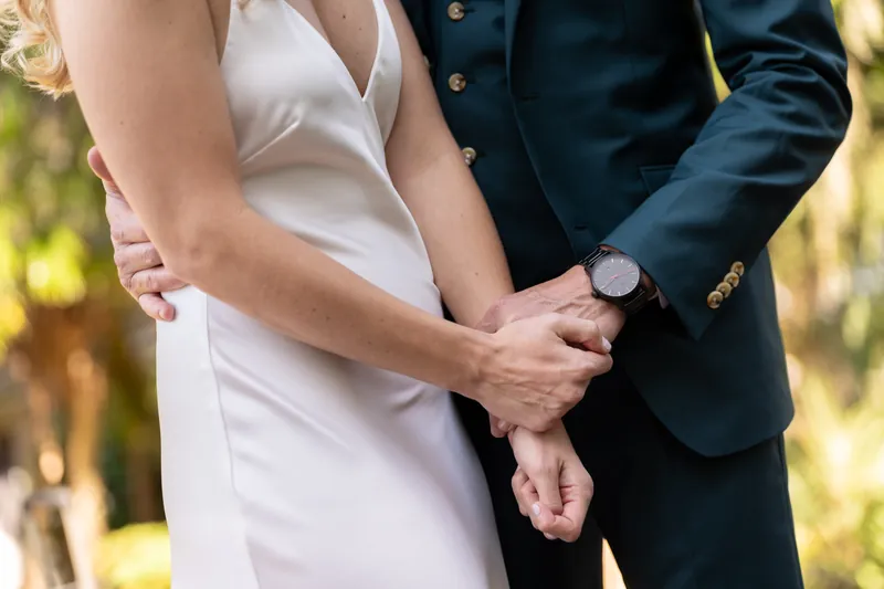 Close view of Kerry and Rhett's clasped hands as they stand together, showing her white gown and his teal jacket.