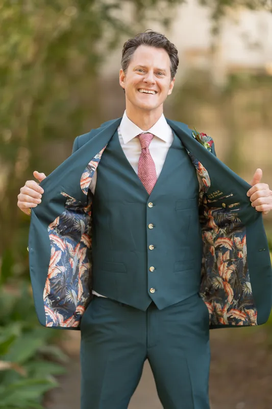 Rhett grins while opening his jacket to reveal a floral patterned lining underneath his formal slate-blue three-piece suit.