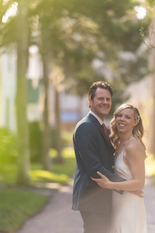 Rhett wraps his arms around Kerry from behind as they pose on the shaded walkway, both smiling toward the camera.
