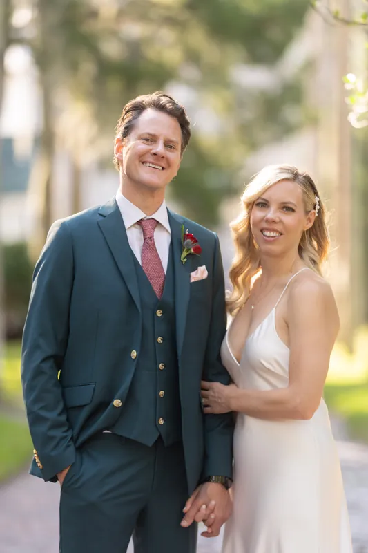 Kerry and Rhett hold hands on a tree-lined path at Casa Monica Resort & Spa, both smiling at the camera in their wedding