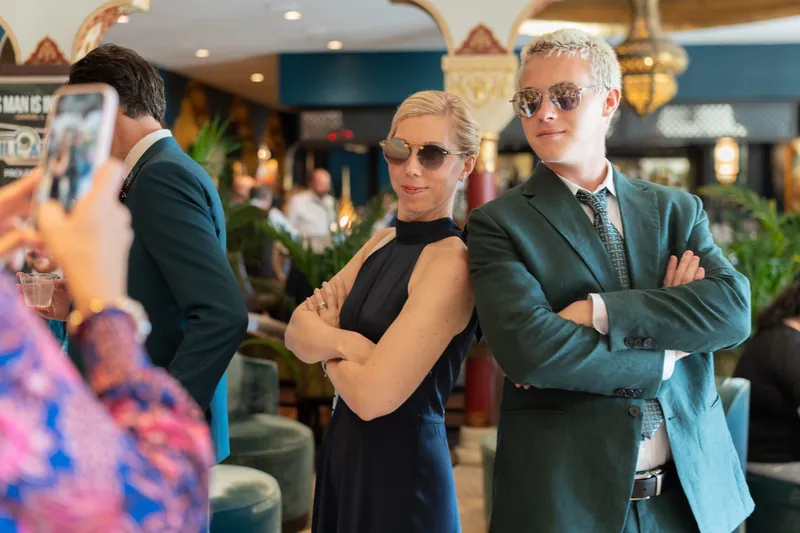 Three guests stand indoors during the reception, the center person in a black sleeveless dress and two others in blazers, all